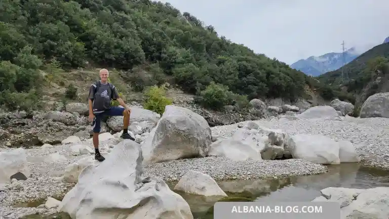 Author standing on a large rock in the Shushicë riverbed surrounded by mountains and cliffs in Albania