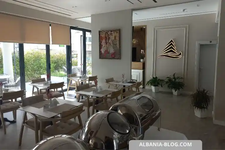 Sea Side hotel breakfast hall in Vlore with floor-to-ceiling windows, tables and green trees outside