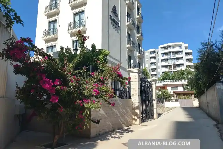 Entrance of Sea Side hotel in Vlore with black metal gates, marble columns and a blooming tree