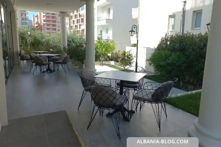 Cozy seating area near the entrance of Sea Side hotel in Vlore with white columns, tables and green trees