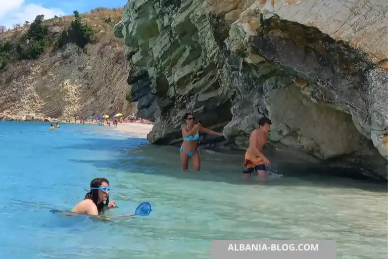 People walking and swimming near rocks at Mirror Beach Ksamil