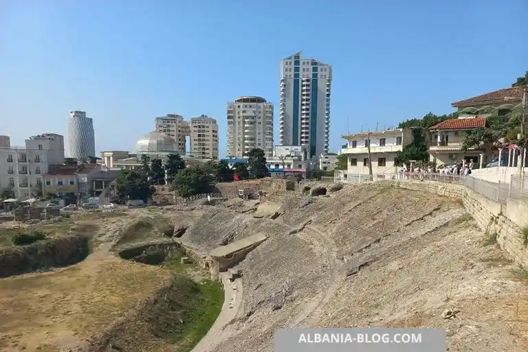 Вид на древний римский амфитеатр в Дурресе на фоне городских зданий