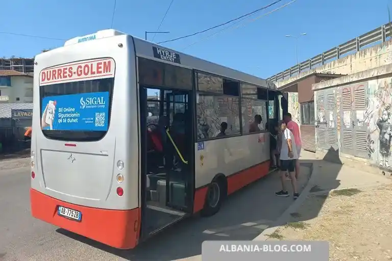 Rear view of Iveco bus with Durre Golem sign at painted bus stop below SH4 highway