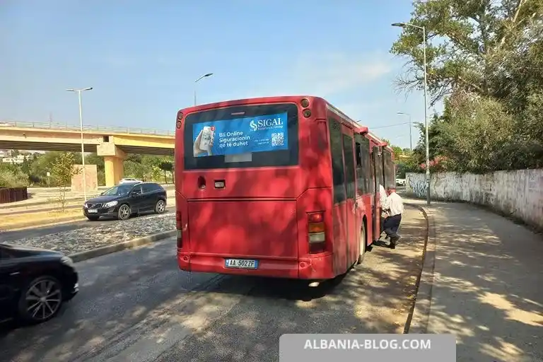 Red intercity bus at Plepa bus stop pocket near white stone wall heading to Golem